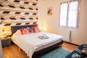 A bedroom with a bed, a nightstand, a lamp, a window with curtains, and a wall with a geometric pattern. - farm house at the foot of the mountains and 1 kilometer from Espelette center (Espelette)