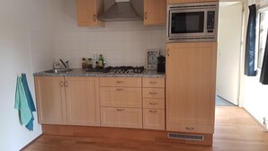 A compact kitchen with wooden cabinets, a microwave, and a gas stove. - Attractive detached house with all amenities and garden / terrace, lots of privacy! (Amerongen)