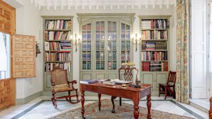 A library with bookshelves, a wooden desk, a rocking chair, and a chandelier.