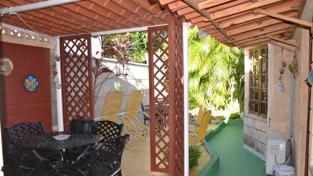 A covered patio with a table and chairs, a small garden area with plants, and a green pathway. - Wacos House in the heart of Varadero (Varadero)