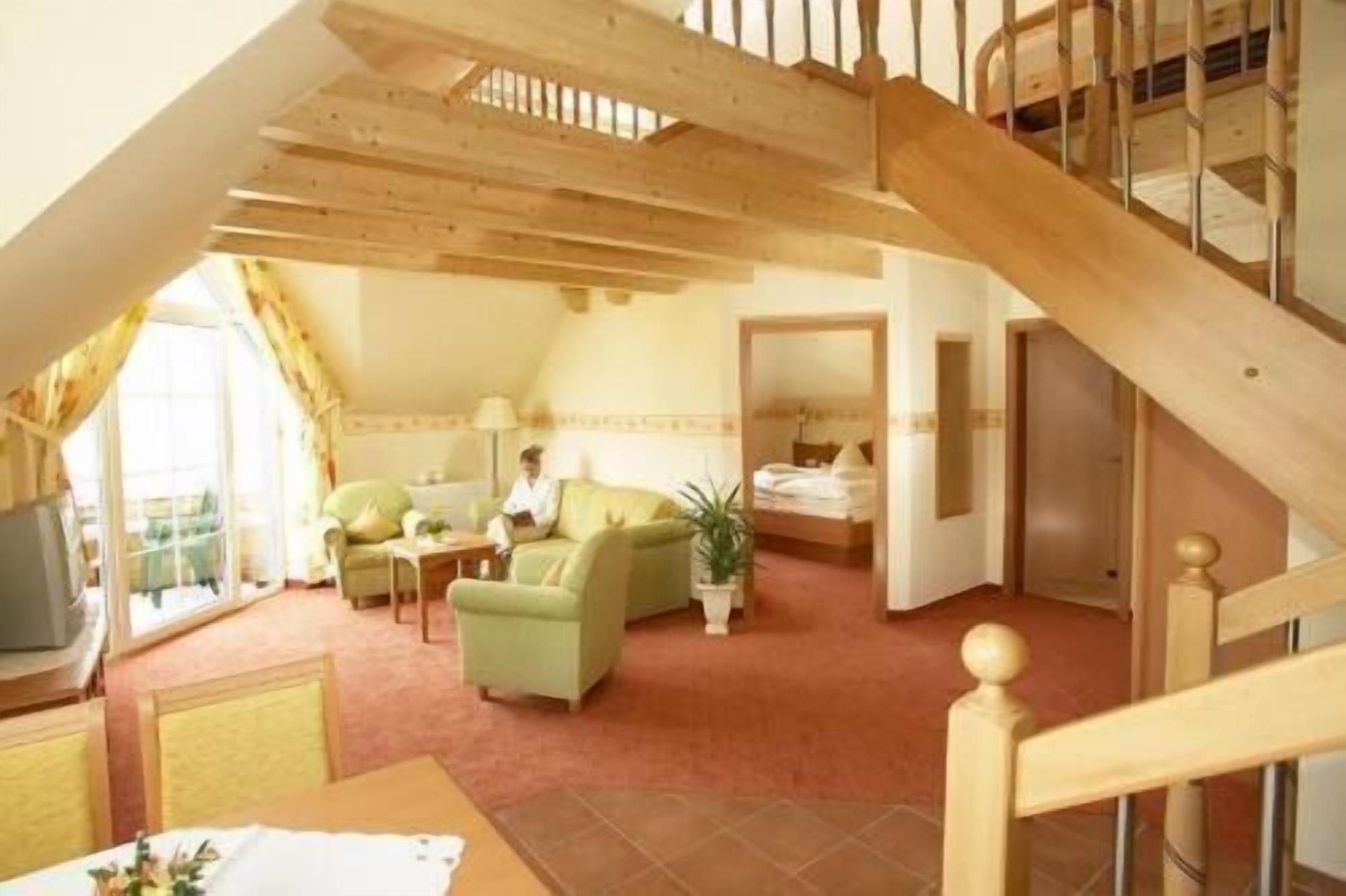 A cozy room with a wooden staircase, a green sofa, a small table, and a bed in the background.