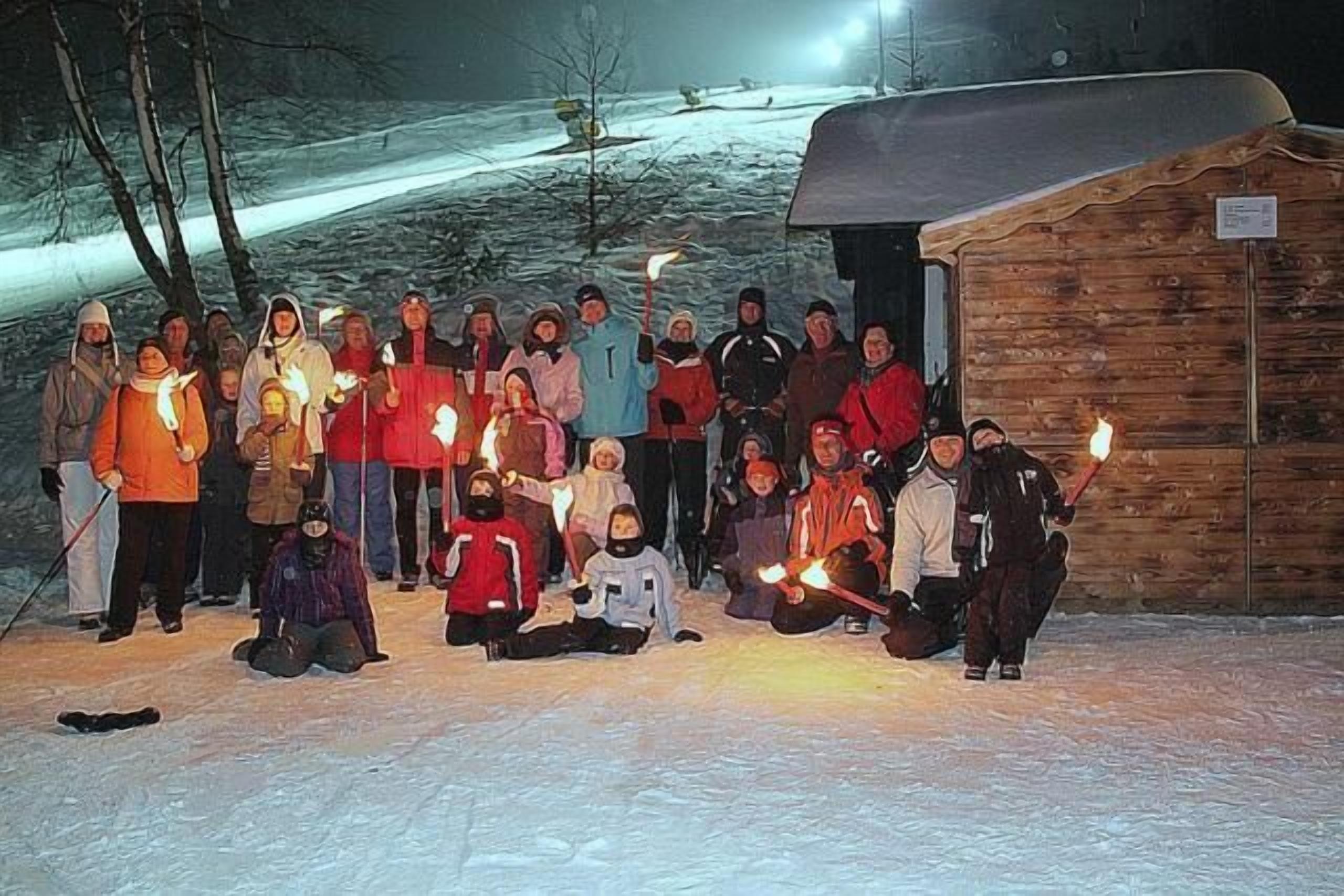 Eine Gruppe von Menschen versammelt sich vor einer Holzhütte in verschneiter Landschaft.