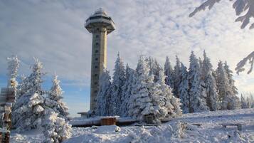A snow-covered tower with a cylindrical shape and a rounded top, surrounded by snow-laden trees and a clear sky.