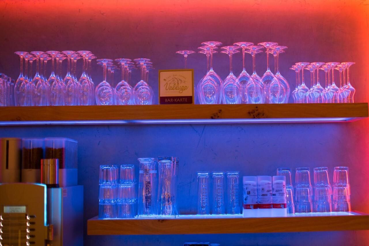 Un espace bar avec des étagères remplies de verres à vin et de bouteilles, éclairé par des lumières rouges et bleues.