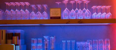 Una zona de bar con estantes llenos de copas y botellas de vino, iluminada con luces rojas y azules.