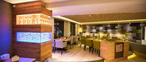 Un restaurante moderno con detalles de madera, una zona de bar y una pantalla digital.