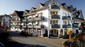 Et hotel med flere etager, en hvid facade, flere balkoner med planter og en rundkørsel.