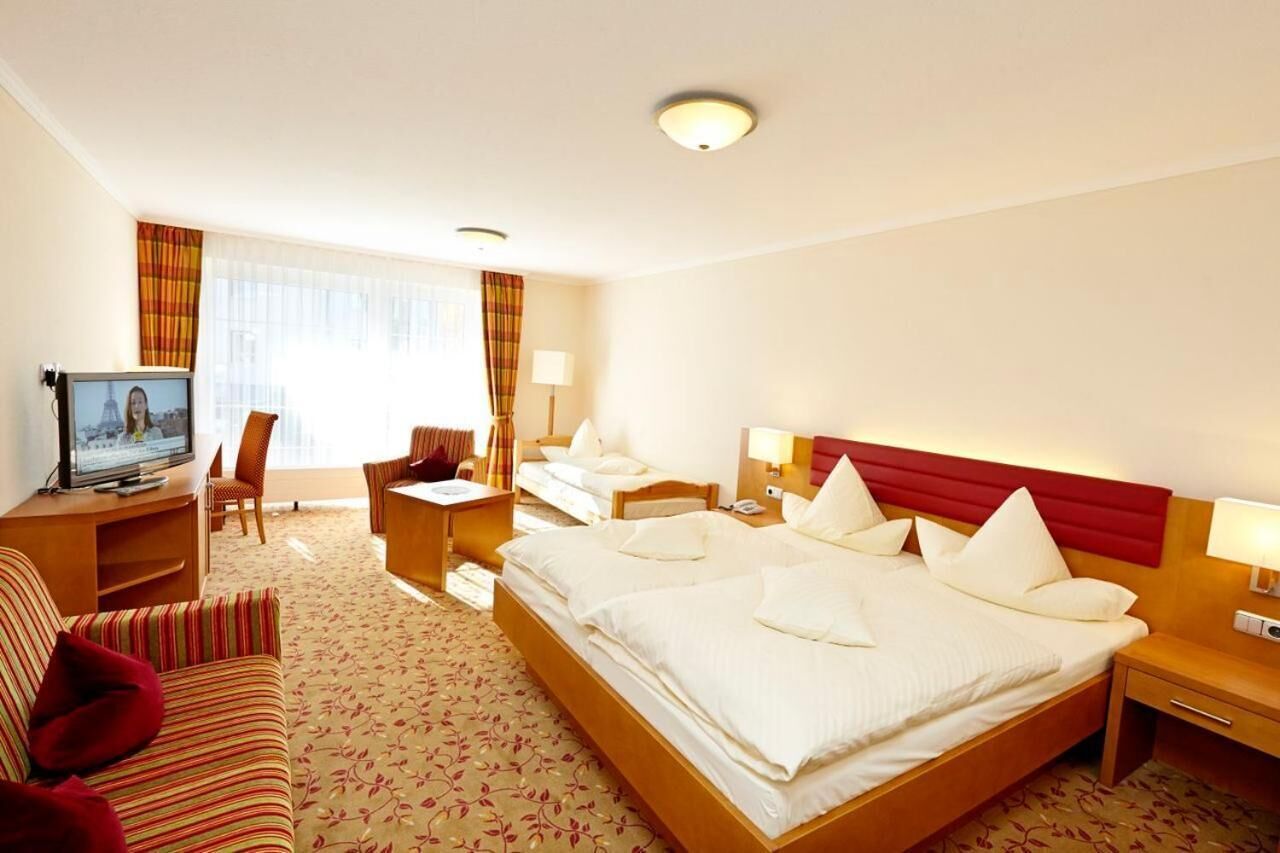 A hotel room with a large bed, a desk, a chair, and a television.