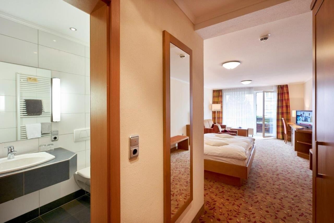 Quarto de hotel com uma cama grande, uma escrivaninha, uma TV e banheiro com pia e espelho.