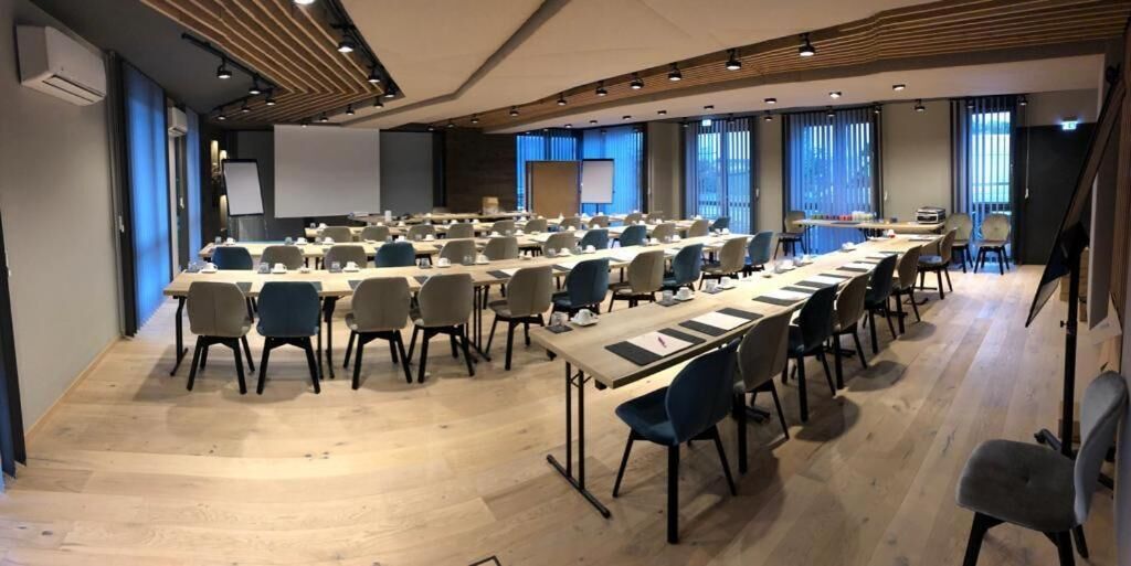 A conference room with multiple tables and chairs, large windows, and a projector screen.