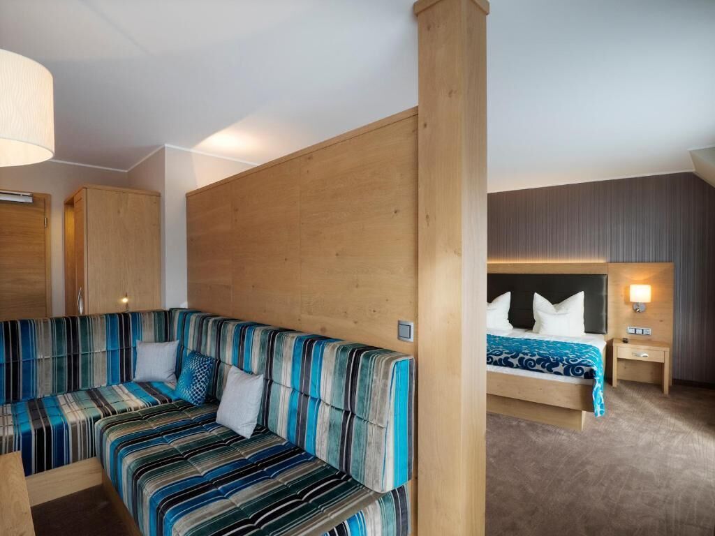 Een kamer met een gestreept bankje, een bed met hoofdeinde en een houten scheidingswand.