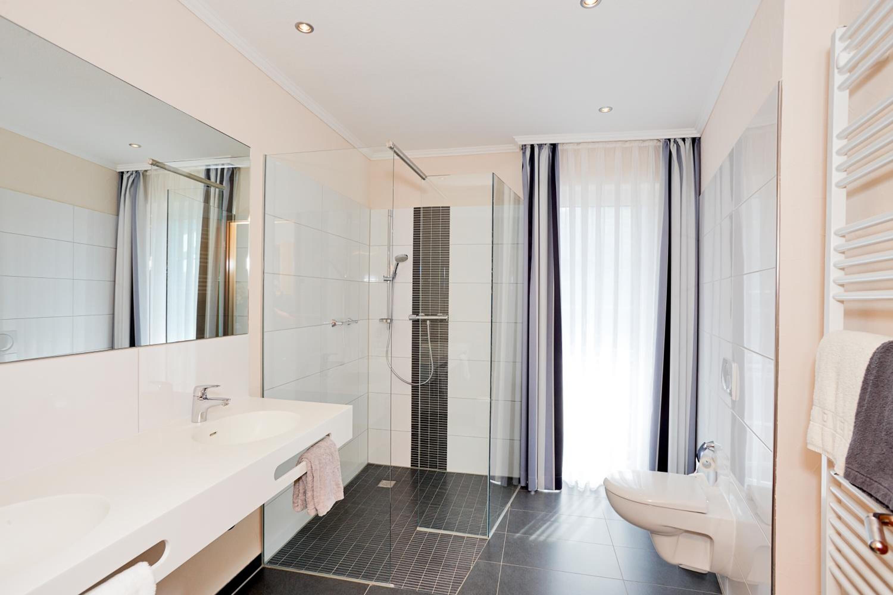 A modern bathroom with a large mirror, a white sink, a glass-enclosed shower, and a toilet.