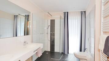 A modern bathroom with a large mirror, a white sink, a glass-enclosed shower, and a toilet.
