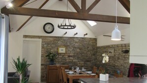 Une cuisine spacieuse avec un mur en pierre, des poutres apparentes et un coin repas avec une table dressée pour quatre personnes.