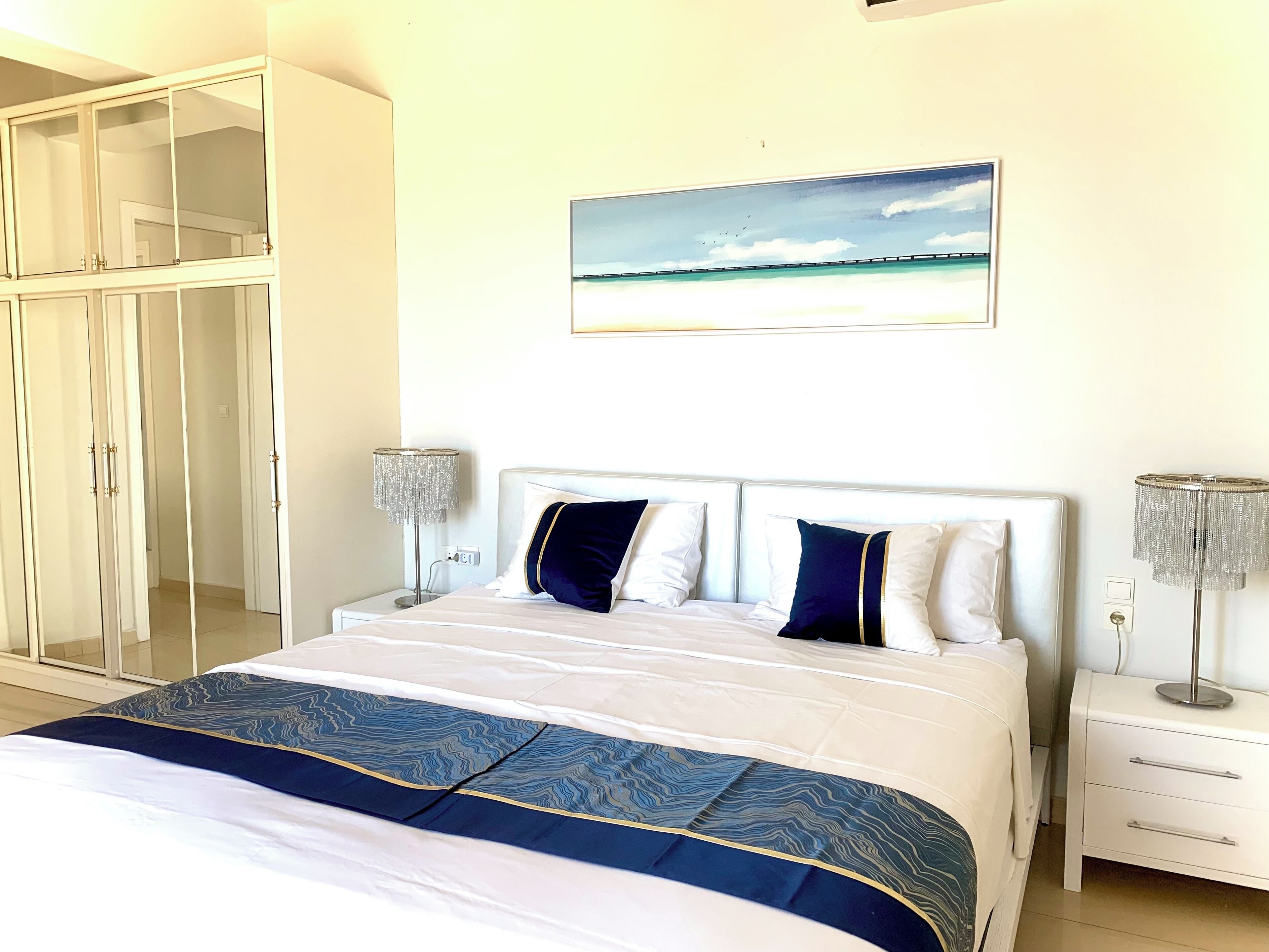 A bedroom with a bed, a wardrobe, a painting, and two bedside lamps.