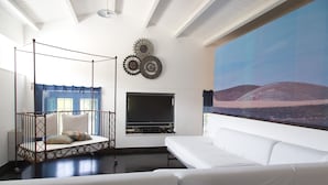 A modern living room with a white sofa, a hanging chair, a flat-screen TV, and a large painting of a desert landscape.