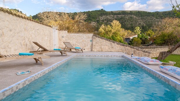 A rectangular swimming pool with a stone wall and a view of a hilly landscape.