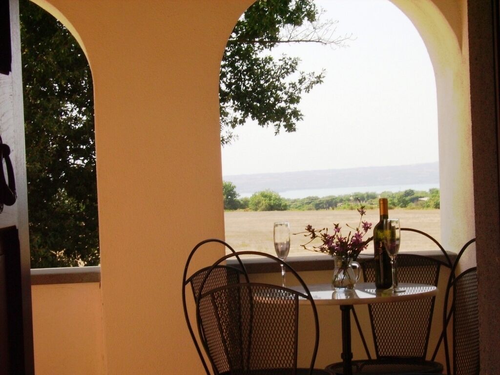 A table with chairs and a bottle of wine, set against a view of a landscape.