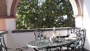 Een terras met een ronde tafel en vier stoelen, een fles wijn en een schaal fruit.