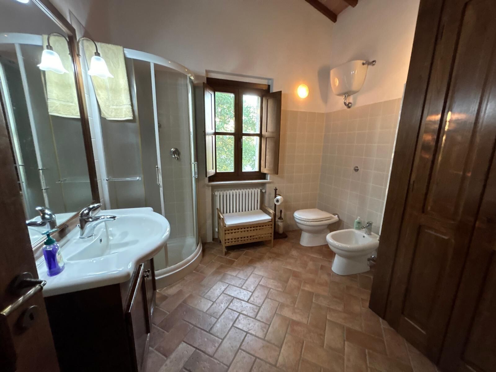 A bathroom with a sink, mirror, toilet, bidet, and a window.