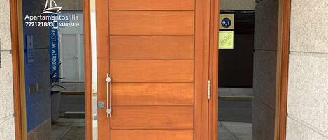 A wooden double door with glass panels, a sign above reading 'Apartamentos Vila,' and a sign indicating 'Rúa Naval, 4 - Portal 3.'