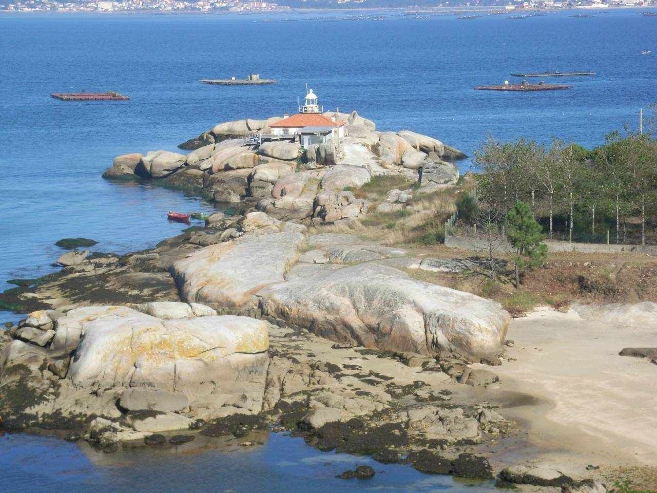 Un rivage rocheux, avec un phare et des bateaux en arrière-plan.