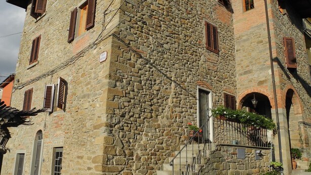 Un edificio de piedra con una escalera que lleva a una puerta, rodeado de vegetación y un camino adoquinado.