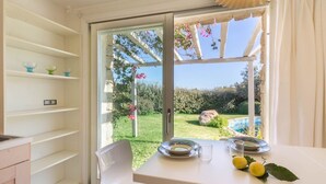 Ein Essbereich mit Tisch für zwei Personen, Blick auf einen Garten durch eine Glastür und ein helles Interieur mit Regalen.