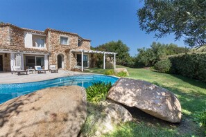 Une maison en pierre avec une piscine, un espace salon extérieur et une pergola.