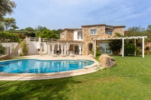 Ein Steinhaus mit Pool, überdachter Terrasse und gepflegtem Rasen.
