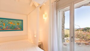 Ein Schlafzimmer mit einem Bett, einem Wandbild, einem Nachttisch und einem Fenster mit Blick ins Freie.