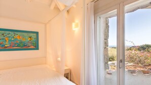 A bedroom with a bed, a wall-mounted painting, a bedside table, and a window with a view of the outdoors.