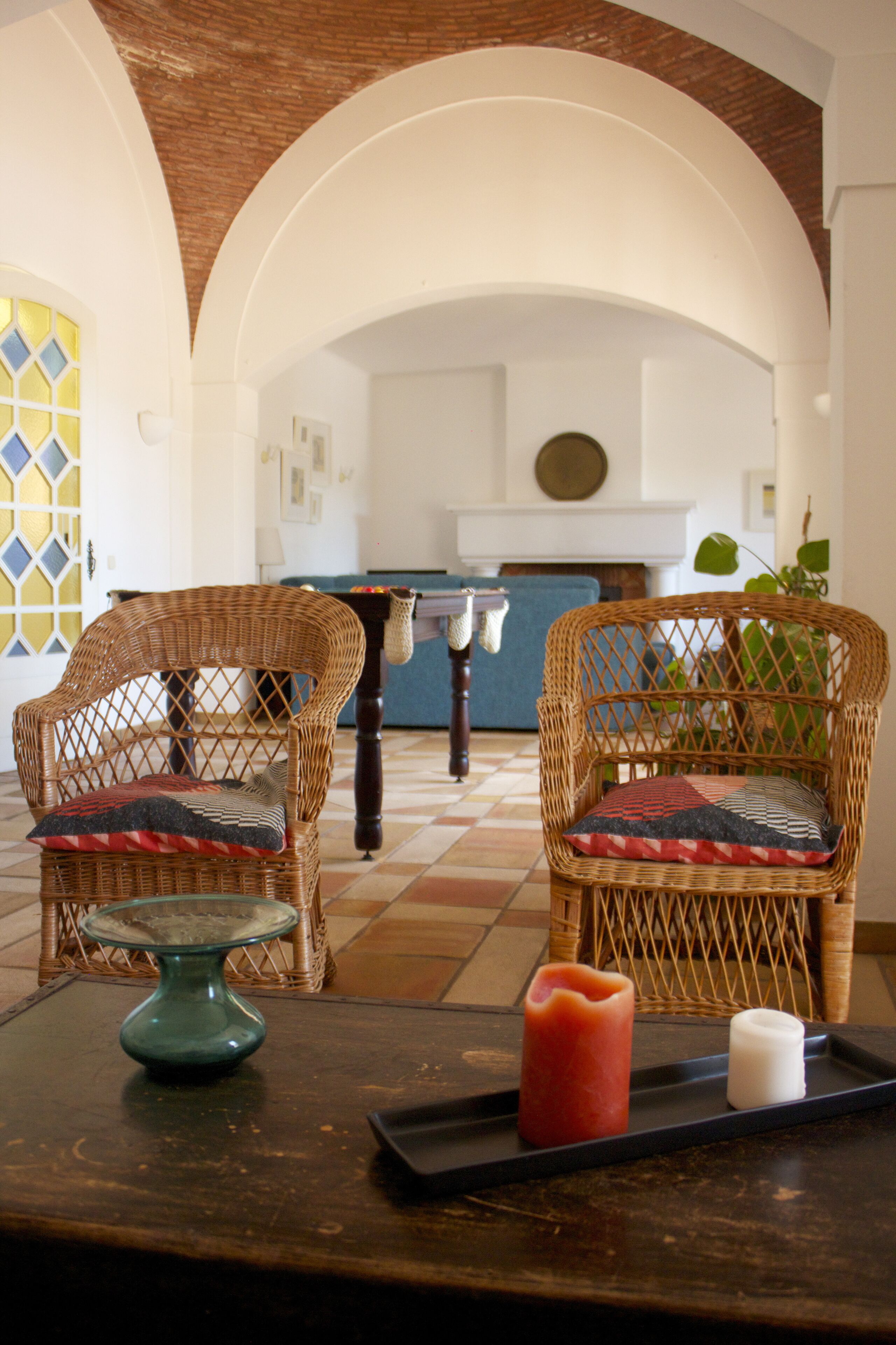 A room with two wicker chairs, a table with candles, and a tiled floor.