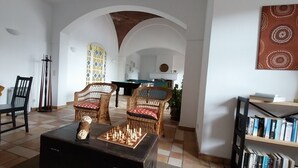 A living room with a chessboard, two wicker chairs, a bookshelf, and a view through an arched doorway to a kitchen. - Large villa - 6 rooms, garden and swimming pool in Budens, near Salema beach.  (Budens)