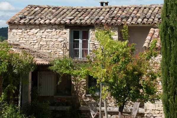 A stone building with a tiled roof, a window with curtains, and a small porch area. - Charming house with swimming pool in the middle of vineyards in Luberon (Goult)