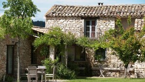 Un bâtiment en pierre avec un toit en tuiles, une terrasse avec une table et des chaises, et un petit jardin.