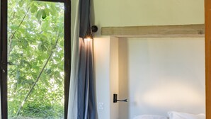 Une chambre à coucher avec un lit, une fenêtre avec des rideaux et une vue sur la verdure à l’extérieur.