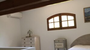 Une chambre à coucher comprenant un lit, une commode, une table de chevet, une fenêtre et un appareil de climatisation.