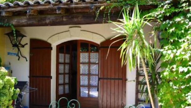 Il s’agit d’un bâtiment traditionnel doté d’une façade en bois, d’un toit recouvert de tuiles et d’un petit jardin agrémenté d’une chaise en métal et d’une plante en pot.