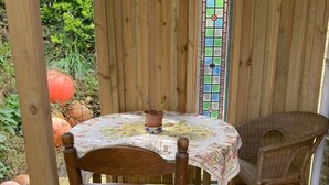 A wooden table with a floral tablecloth, a wicker chair, and a potted plant on a wooden deck.