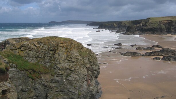 A coastal landscape with rocky cliffs and a sandy beach.
