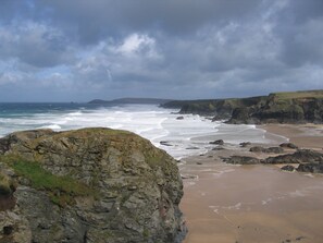 A coastal landscape with rocky cliffs, a sandy beach, and the ocean under a cloudy sky. - Cosy with a real Cornish feel right on the beach, near Padstow. (Padstow)