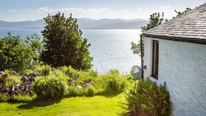Een wit huis met een stenen dak, een gazon en uitzicht op een groot wateroppervlak en bergen in de verte.