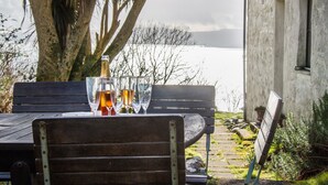 Een houten bank met een tafel voor twee, bierglazen en een fles wijn, met uitzicht op een wateroppervlak en een gebouw.