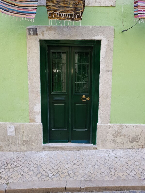 Una porta verde a due ante con maniglia in ottone, incorniciata in pietra, su un muro verde con un piccolo cartello sopra.