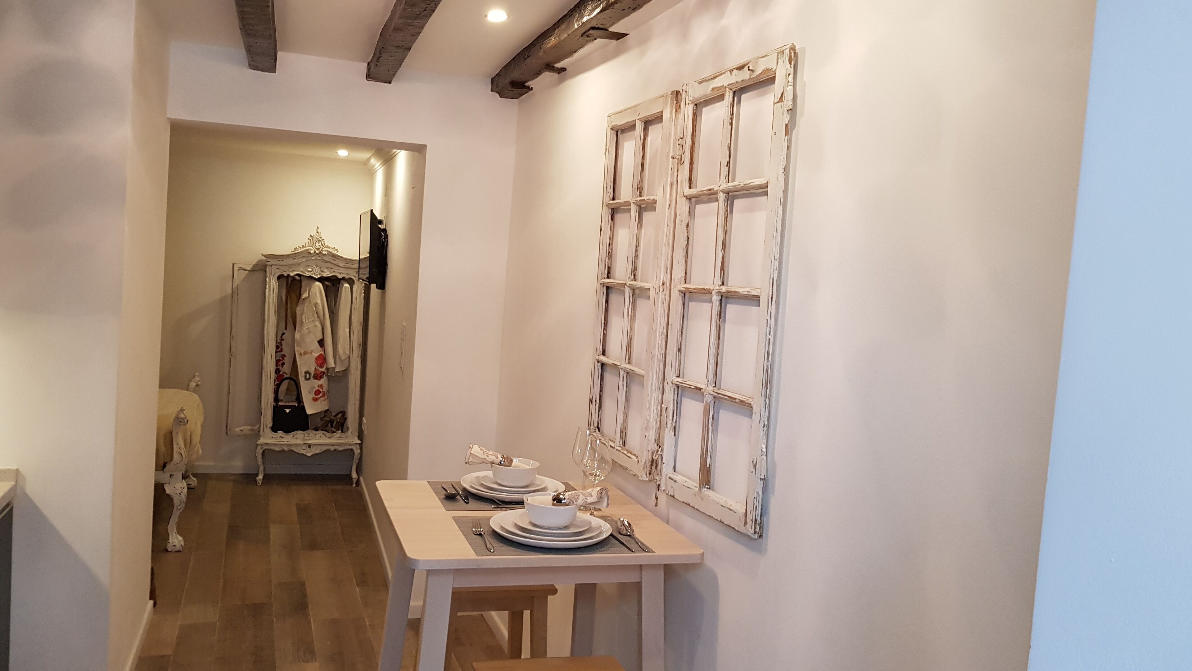 Un pasillo estrecho con una mesa puesta para comer, un espejo con marco decorativo y una puerta rústica.