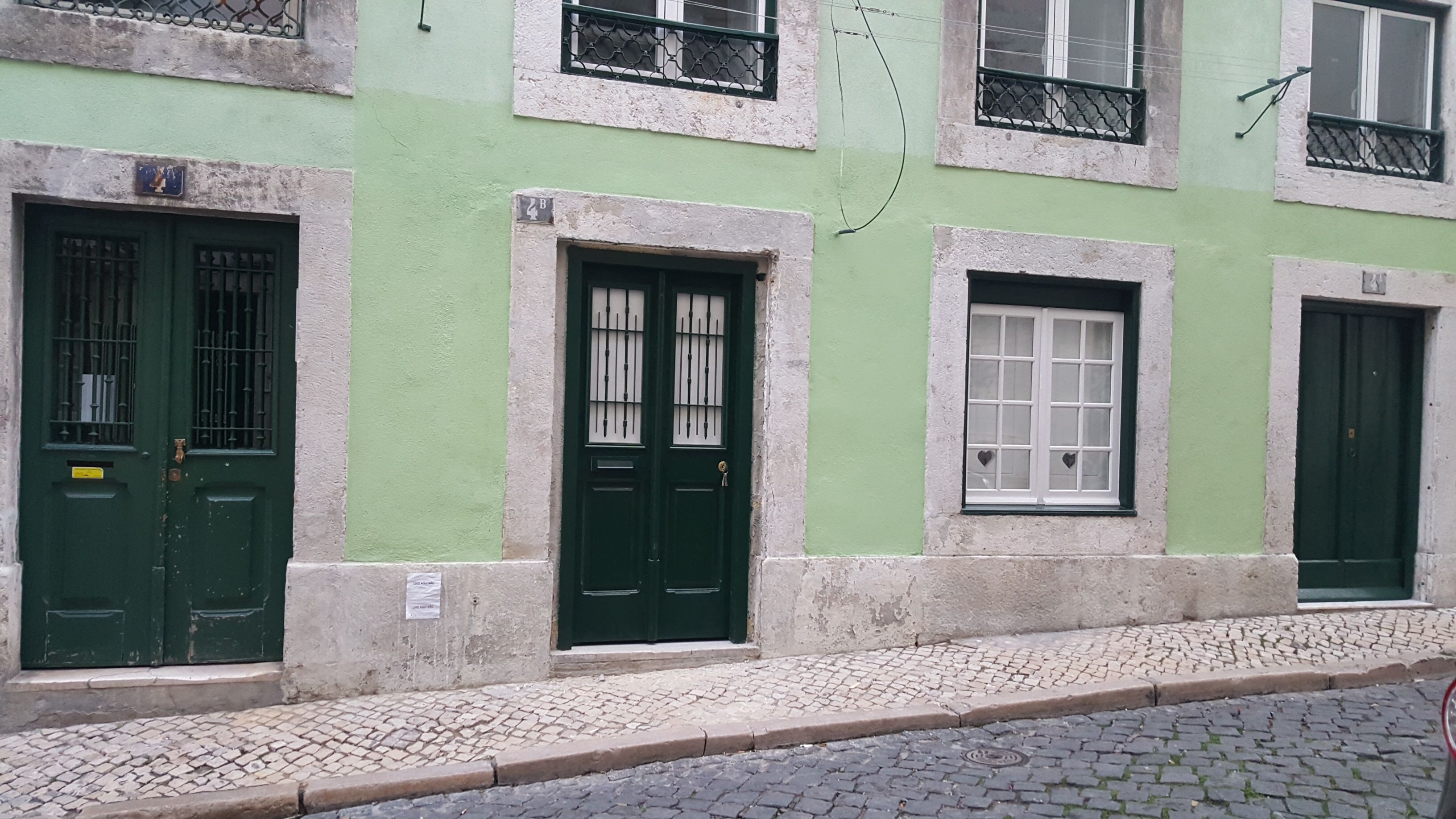 A building with green doors and windows, a cobblestone street, and a metal fence.