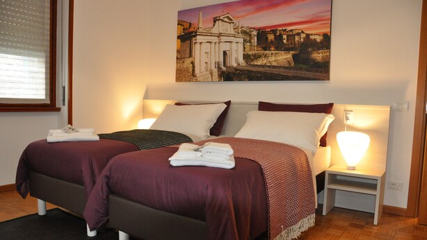 Une chambre d’hôtel avec deux lits, une table de chevet avec une lampe et un tableau représentant un bâtiment historique accroché au mur.