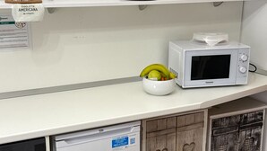Une cuisine avec un réfrigérateur blanc, un four à micro-ondes et un petit saladier de fruits posé sur le comptoir.