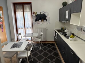 A compact kitchen with a dining table, chairs, a radiator, and a wall with pinned notes.